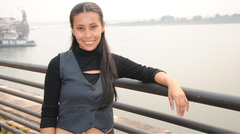 A young woman stands in front of a body of water.